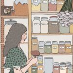 A woman is standing in her pantry. She has long, dark hair and is wearling a green top. There are shelves behind her filled with jars of dry goods.